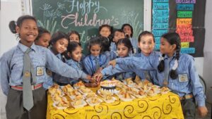 A group of children gathered around a table of snacks smile at the camera with a chalkboard in behind them with the words Happy Children's Day