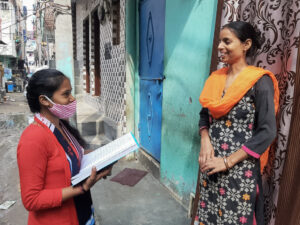 A Child Champion stands in a narrow street outside a brightly painted house talking with a mother