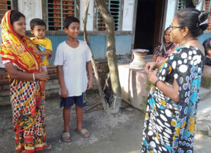 A mother holding her baby and her young teen son smile as they talk with a visiting Child Champion in front of their home 