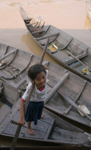 A small girl in Cambodia looks up at the camera as she stands barefoot in a fishing boat
