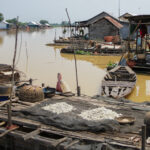 Boats and floating shanties mark a floating fishing village on a muddy lake in Cambodia
