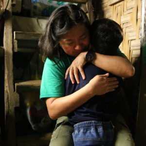 Manette Cosico hugs a small child while sitting on the lower stop of a crude wooden ladder