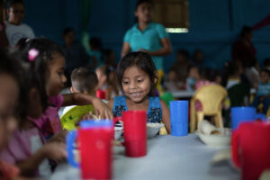 A little talks with friends at a lunch table set with plastic cus and bowls at a Hope Center in Nicaragua