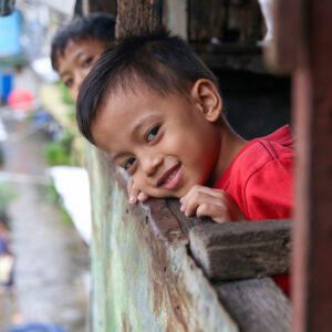 A boy in a red shirt peers over the edge of a ramshackle balcony