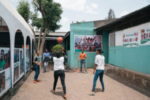 Five youth playing vollyball in front of teal colored cement building