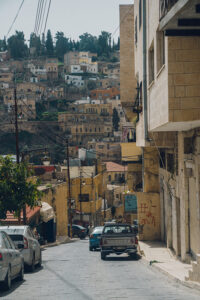 An older model pickup is parked on a steep cobblestone street in Jordan lined with brick buildings marked with graffiti