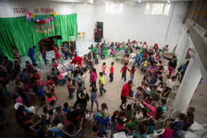 Overhead view of a celebration at a hope center as kids mingle and play in a large room decorated with balloons