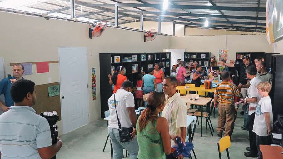 Adults and youth looking around a room with a metal ceiling containing with bookcases on three walls and tables and chairs in the middle.