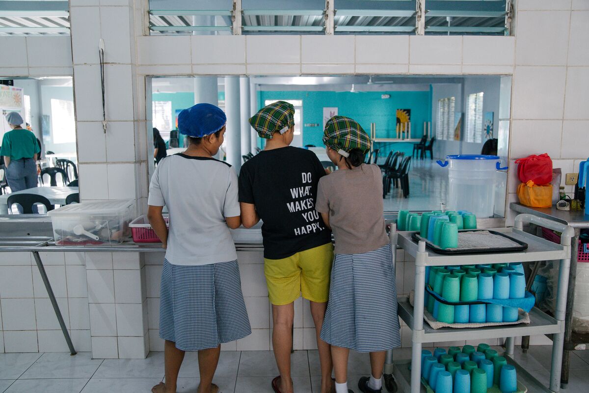 Three teen girls in hair nets stand at a dining serving line with their backs to the camera. 