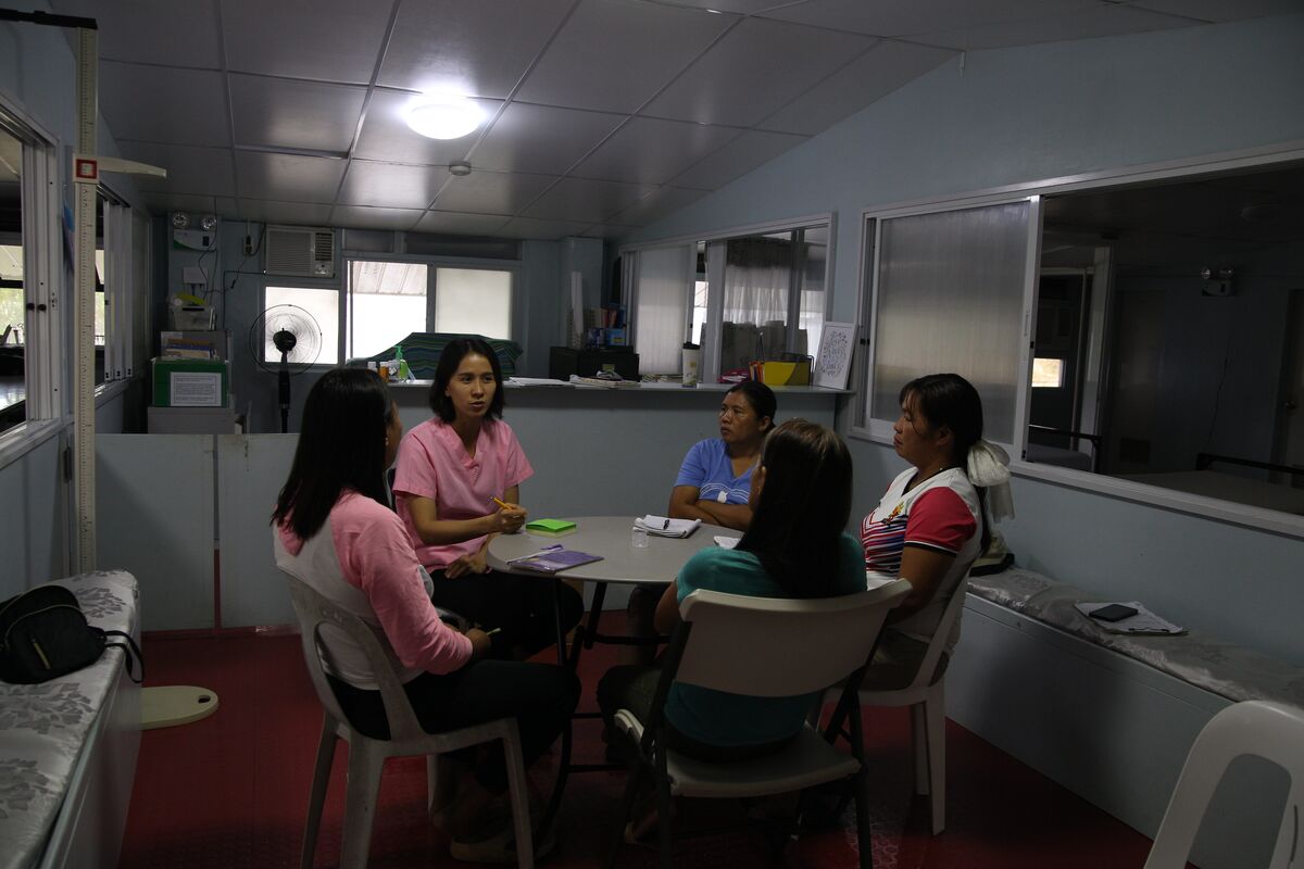 5 women sit around a table in a small office. 