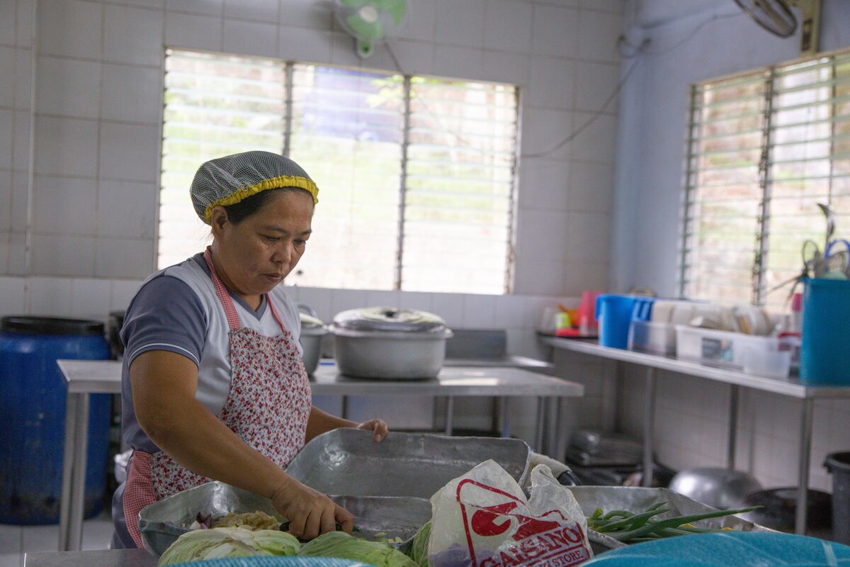 A woman in an apron and hair net fills a pan with vegetables in an industrial kitchen