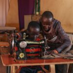 A man helps show a boy how to use an treadle sewing maching at a hope center in turkana kenya