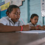 Girls study at a wooden desk in a classroom in cambodia