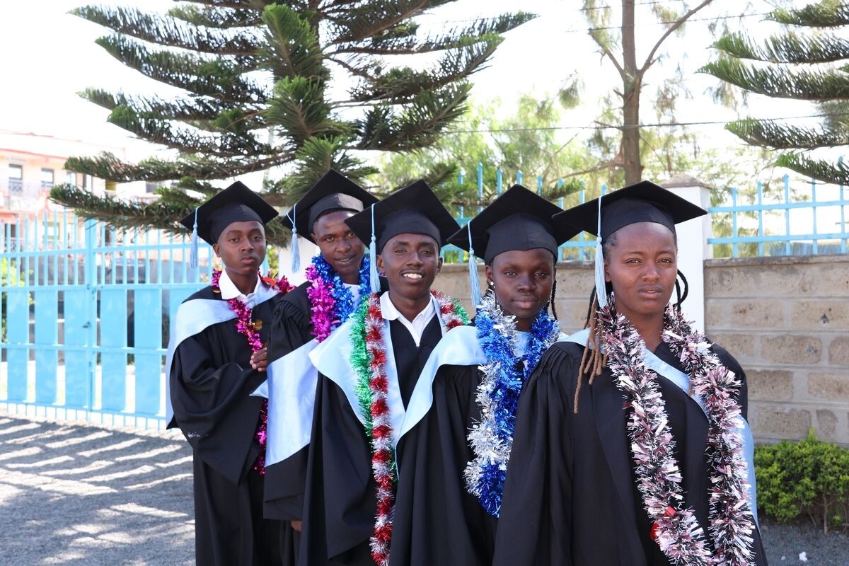Five graduates in caps and gowns line up in a row.